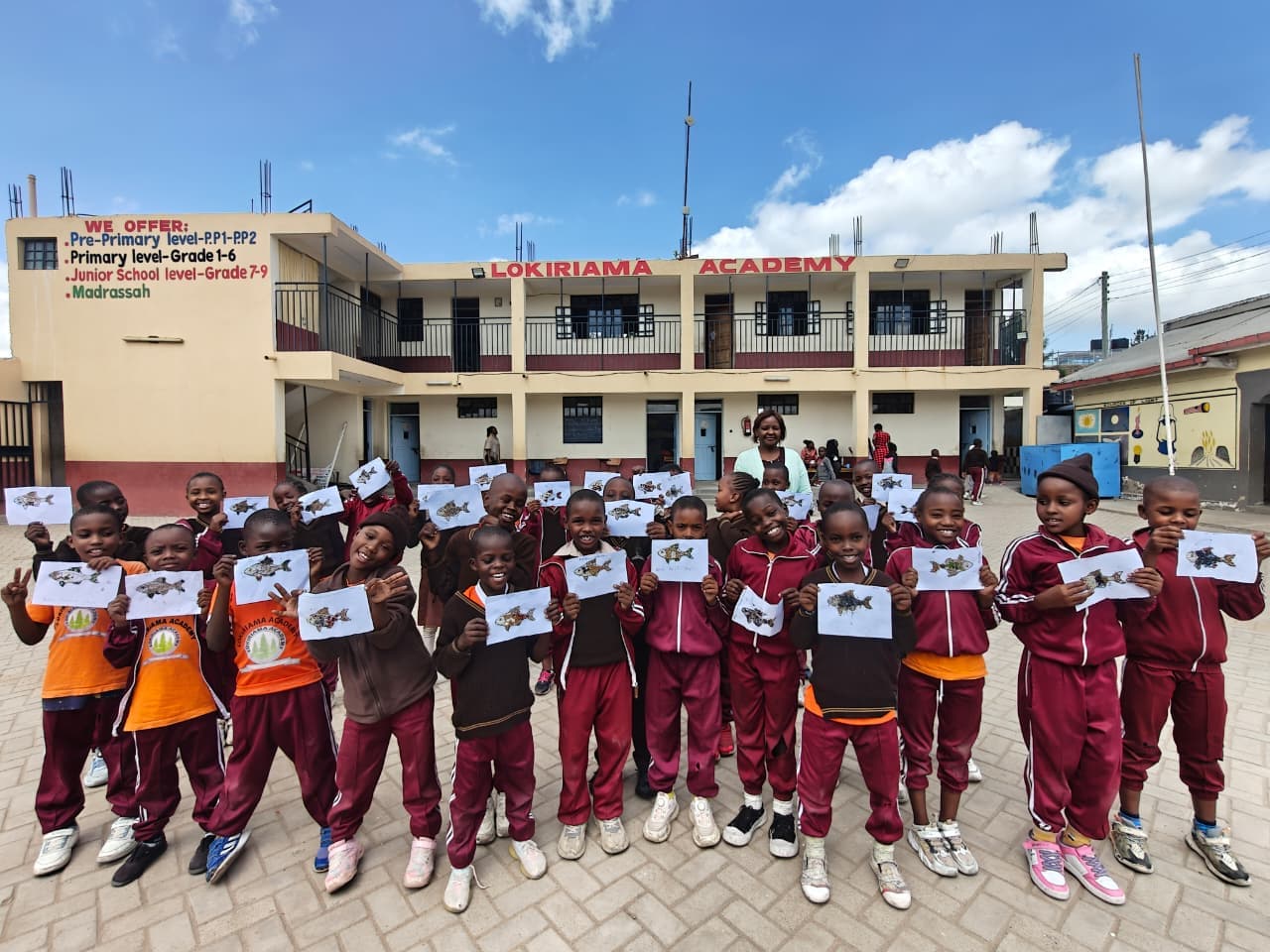 Learners holding up their outdoor artwork in front of the school block